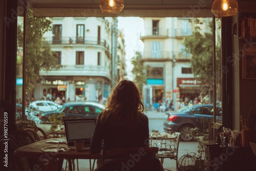 Woman working on laptop in cafe, looking at city street scene