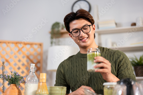 Asian young man drinking matcha tea at table in bright, cozy house.
