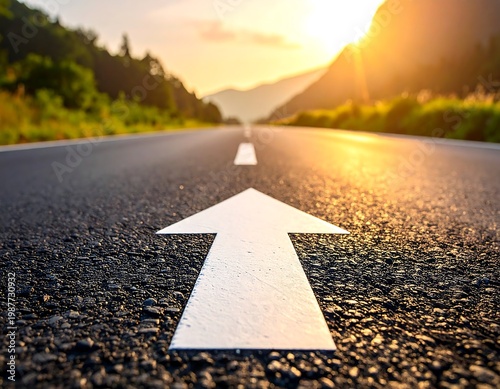 A close-up view of an asphalt road leading towards the sunrise, with an arrow marking direction. Mountains and trees are on the sides