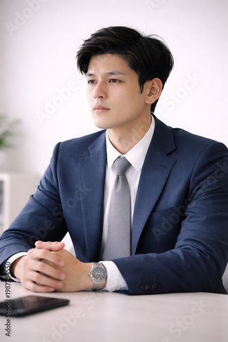 Young Asian businessman wearing suit tie corporate office portrait feeling focused and professional sitting at table desk during meeting