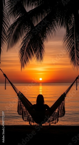 Silhouette of person relaxing in hammock under palm trees at sunset over ocean.