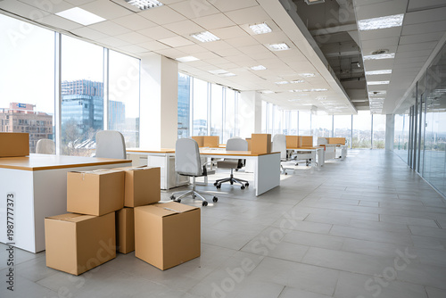 A spacious, bright, modern office interior with large windows, desks, chairs, and cardboard moving boxes