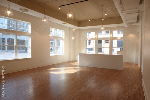 An empty, brightly lit interior space with large windows overlooking a city street. Wooden flooring and a white bar are present