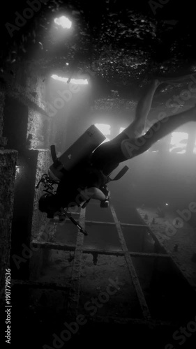 Courageous scuba diver swimming inside a dark, rusty shipwreck illuminated by sunbeams