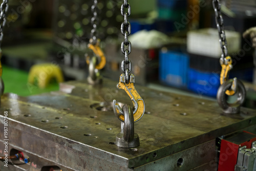 Yellow hoist hook hangs above steel lifting eye on mold surface, ready for controlled lifting, safe die handling, and maintenance workflow during production changeover in factory workshop line