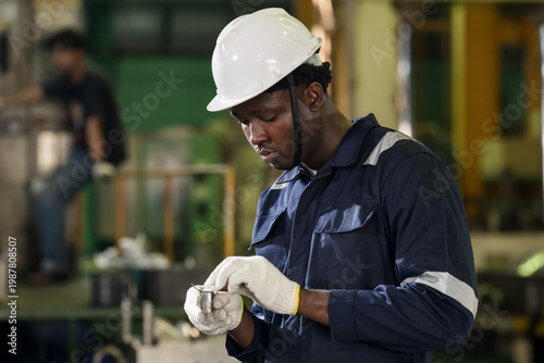 Photos African male technician adjusts glove beside production area, preparing for next task in factory workshop and showing PPE readiness, workplace safety, and maintenance support before operation