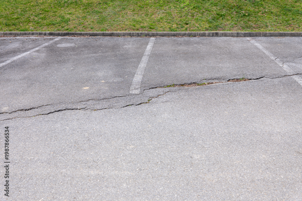 Obraz premium Damaged asphalt in a parking lot with cracks and deteriorated surface, infrastructure and maintenance problem in urban environment.