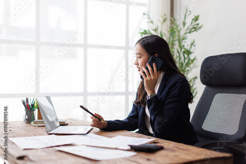 Tableau sur toile Asian businesswoman multitasking in a modern office with devices