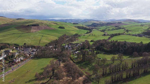 Traditional Scottish village of Eddleston surrounded by green farmland and rolling hills near Peebles. Scenic rural landscape featuring country houses and agricultural fields in Scotland.