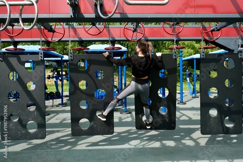 A girl is completing a suspended obstacle course at a street workout area. OCR (Obstacle Course Racing)
