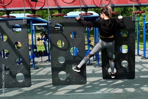 A girl is completing a suspended obstacle course at a street workout area. OCR (Obstacle Course Racing)
