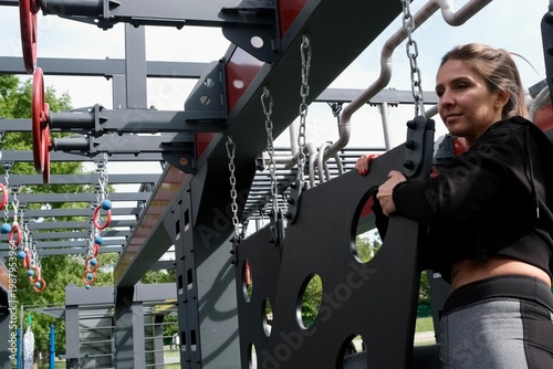 A girl is completing a suspended obstacle course at a street workout area. OCR (Obstacle Course Racing)
