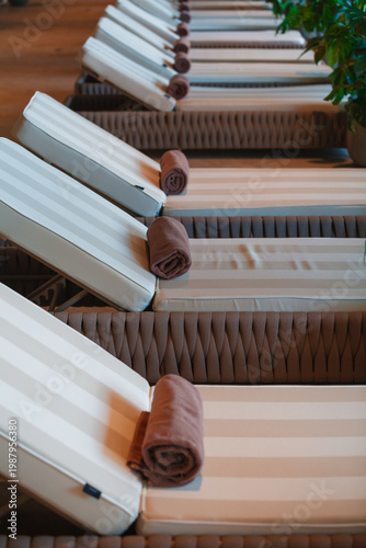 Premium indoor spa relaxation zone with row of empty sun loungers and rolled towels. Luxury wellness hotel interior background