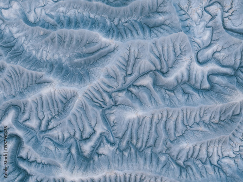 Aerial view of intricate eroded badlands and mudstone formations around Factory Butte showing deep ridges, gullies, and a dendritic drainage pattern in Wayne County, Utah, United States.