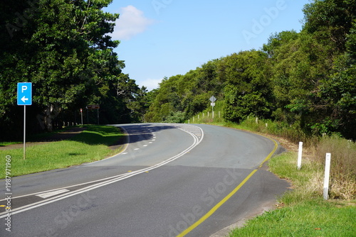 Winding rural road in Australian forest landscape with bright sky and roadside markers