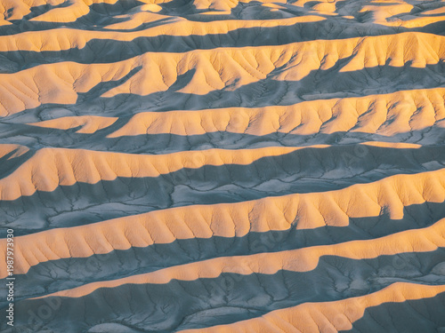 Aerial view of the intricate eroded ridges and badlands at the base of Factory Butte during golden hour in Wayne County, Utah, United States.