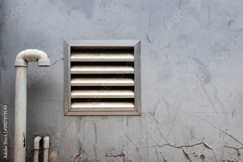Old gray wall with air ventilation grill and plumbing vent pipe background