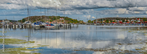view on Fjalbacka village at the horizon with boats in marina under  cloudy blue sky ireflecting on the water surface in sweden