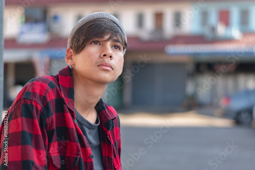 A quiet moment of melancholy. This middle schooler, dressed in a red plaid shirt and a grey knit hat, stands alone with a sad, introverted expression. Capturing the complexity of youthful solitude.