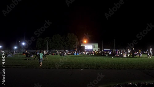 Large Crowd Watching a Movie at an Outdoor Open-Air Cinema Event on a Grass Field at Night