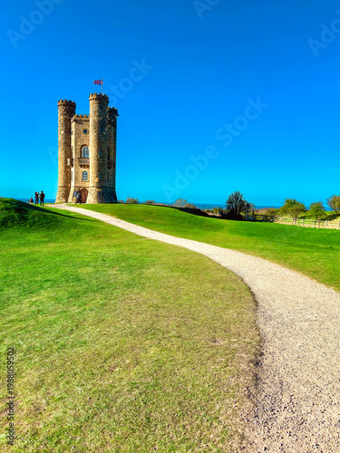 Fotografija The historic Broadway Tower folly at golden hour with a couple resting on a benc
