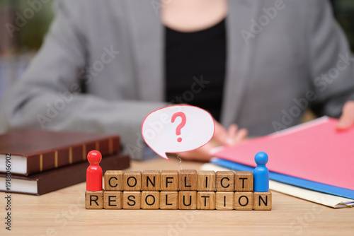 Individuals engage in a thoughtful dialogue about conflict resolution using colorful figures and blocks on a wooden table. Files and legal books hint at a serious discussion.