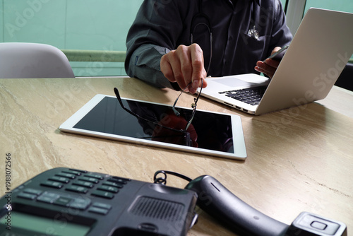 Doctor Using Tablet and Laptop at Desk with Medical Equipment