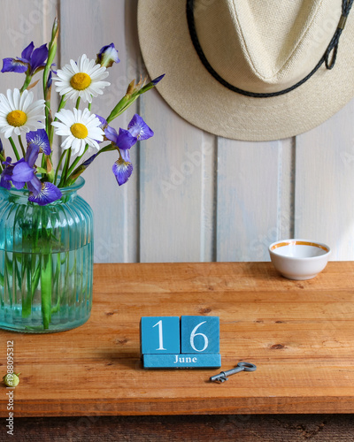 summer still life with calendar showing June 16 flowers in glass vase straw hat and rustic home decor