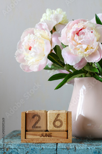 June 26. calendar and bouquet of garden peonies in a mug on the table in the cottage. summer holiday, event, or deadline.