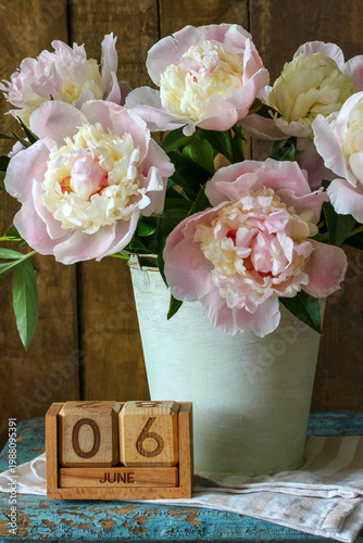 June 6th. a calendar and a bouquet of garden peonies in a bucket on the table in the cottage. summer holiday, event or deadline.