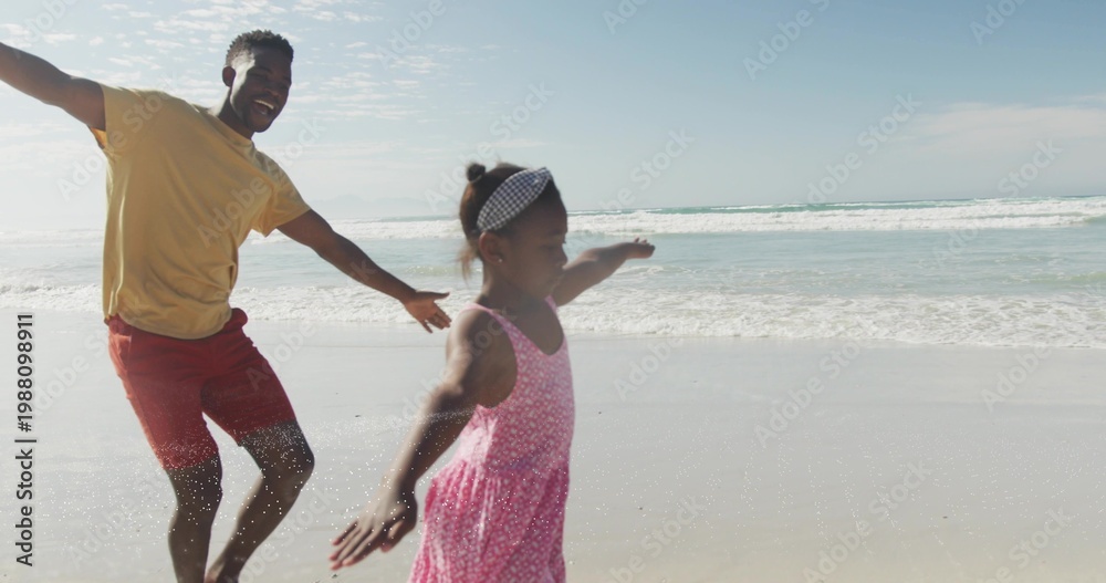 Obraz premium Running father and daughter mirroring poses, splashing surf at beach with wet sand and pink dress