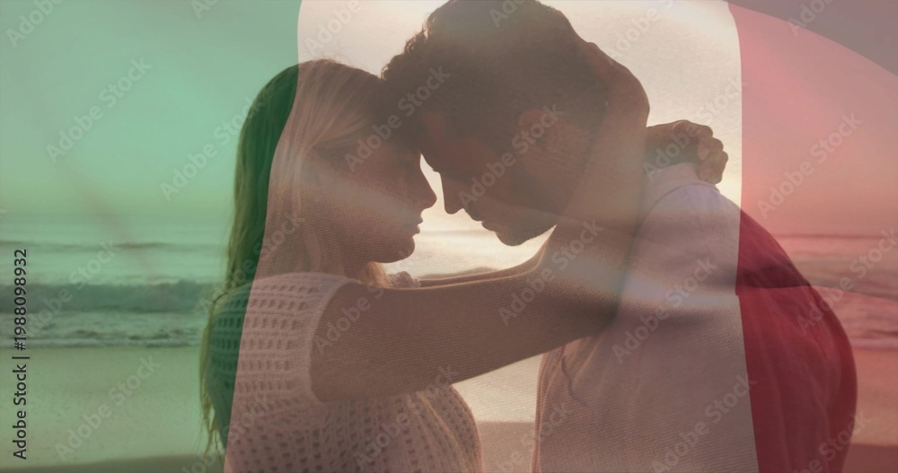 Fototapeta premium Embracing couple in knit top, red jacket leaning heads at beach wet sand, with color overlay