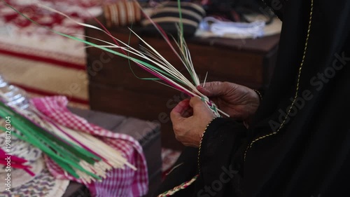 Emirati woman weaving traditional basket from palm leaves, hands in frame, closeup