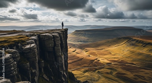 Lone figure stands on a dramatic cliff edge overlooking a vast valley