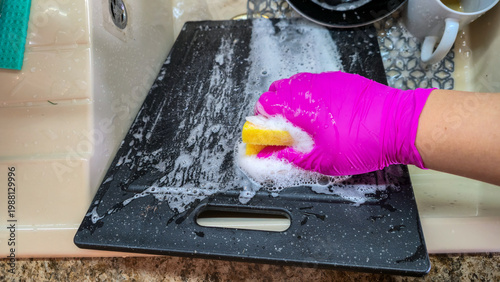 Bild auf Leinwand wide view of pink rubber gloved hand washing large black plastic cutting board w