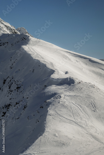 Snow-covered mountain slopes in winter with clear blue sky and trails at a ski resort in the afternoon. Tatra mountains, Zakopane, Poland