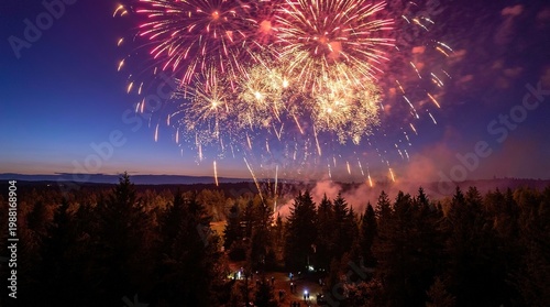 Fireworks display over trees and mountains during nighttime celebration with clear blue sky and smoke trails  aerial view