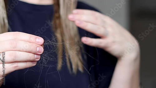 Female with long hair examines strands of hair in hands, showcasing the gradual separation of hair strands in a well-lit indoor setting