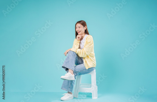 Bild auf Leinwand Happy Young Asian Woman Sitting and Thinking on Turquoise Background