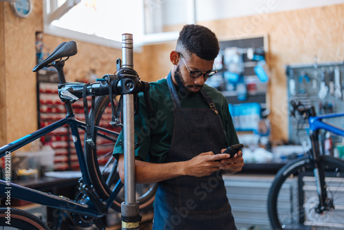 Bild auf Leinwand Bicycle mechanic operating smartphone in workshop