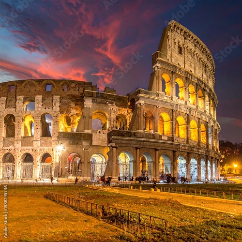 Illuminated ancient amphitheater, showcasing architectural grandeur against a vibrant sunset sky. People stand near structure