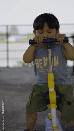 Toddler Sitting And Playing On Scooter, A video of toddler sitting and playing on scooter, gripping handlebars with big smile while scooting slowly, perfect for child play or childhood documentary.