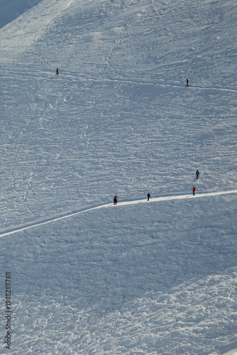 People walk on a snowy mountain slope in bright daylight, engaged in a winter activity on a clear day in the outdoors