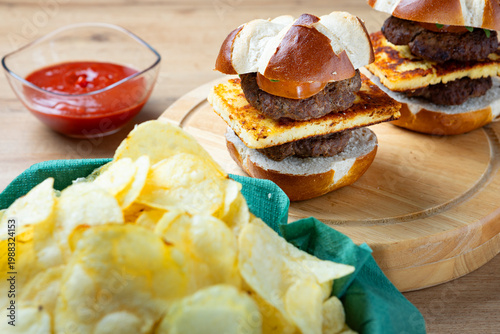 Homemade mini burgers sliders served on wooden board with potato chips and ketchup, shallow depth of field food composition, casual snack or street food concept.