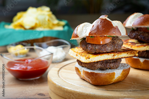 Homemade mini burger sliders with grilled cheese and beef patties on wooden board, served with chips and sauces, appetizing food styling for fast food or casual dining concept.
