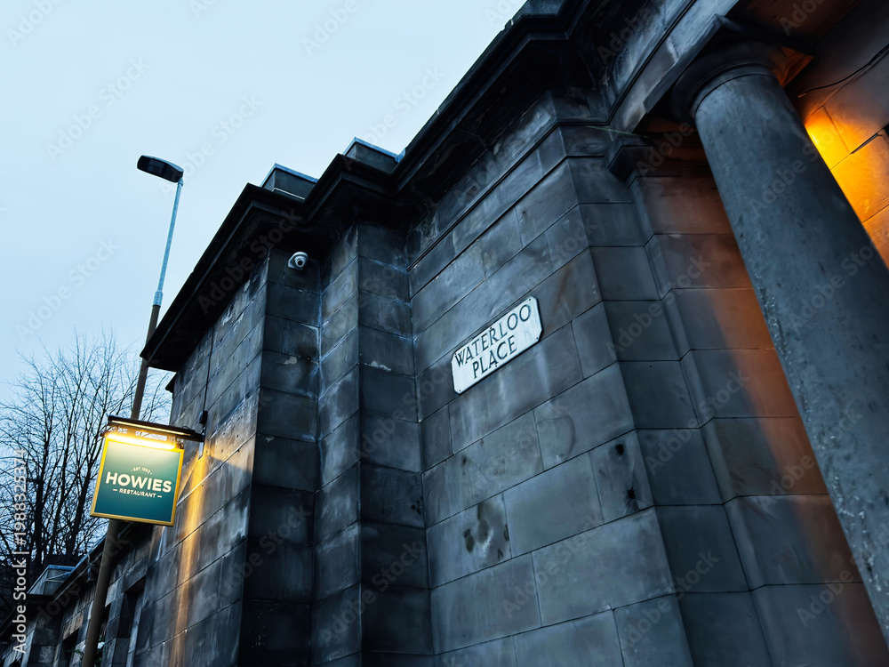 Naklejka premium Evening view of Waterloo Place building facade and Howies restaurant sign in Edinburgh, Scotland, UK with moody blue urban architecture and classical stone columns