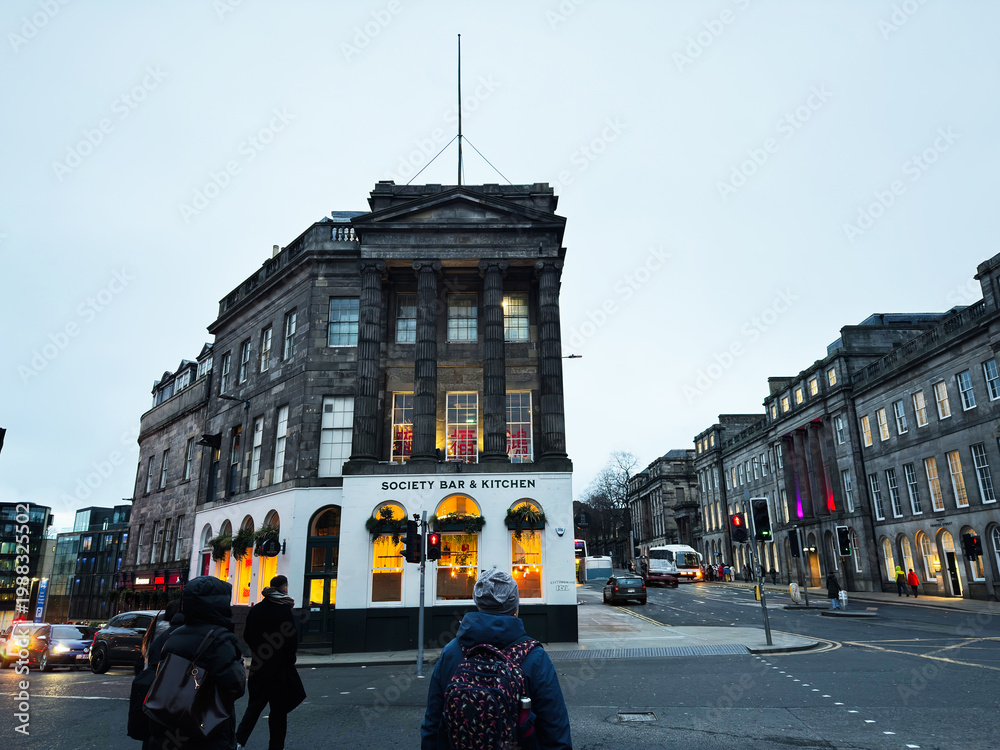 Naklejka premium Evening street scene outside Society Bar and Kitchen in Edinburgh, Scotland, UK with pedestrians, traffic and Georgian architecture