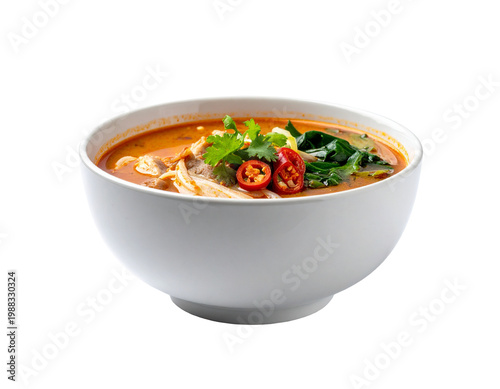 Creamy thai tom yum soup in white bowl with herbs and chili slices