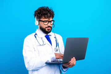 Male doctor conducting a telemedicine consultation on a laptop while wearing a headset and stethoscope, providing virtual healthcare and patient support against a bright blue background