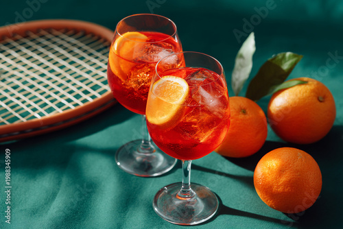 Two Glasses of Refreshing Orange Spritz Cocktail with Tennis Racket in Summer Setting